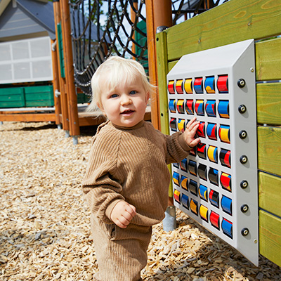 A young child is playing on interactive play panels at a playground.